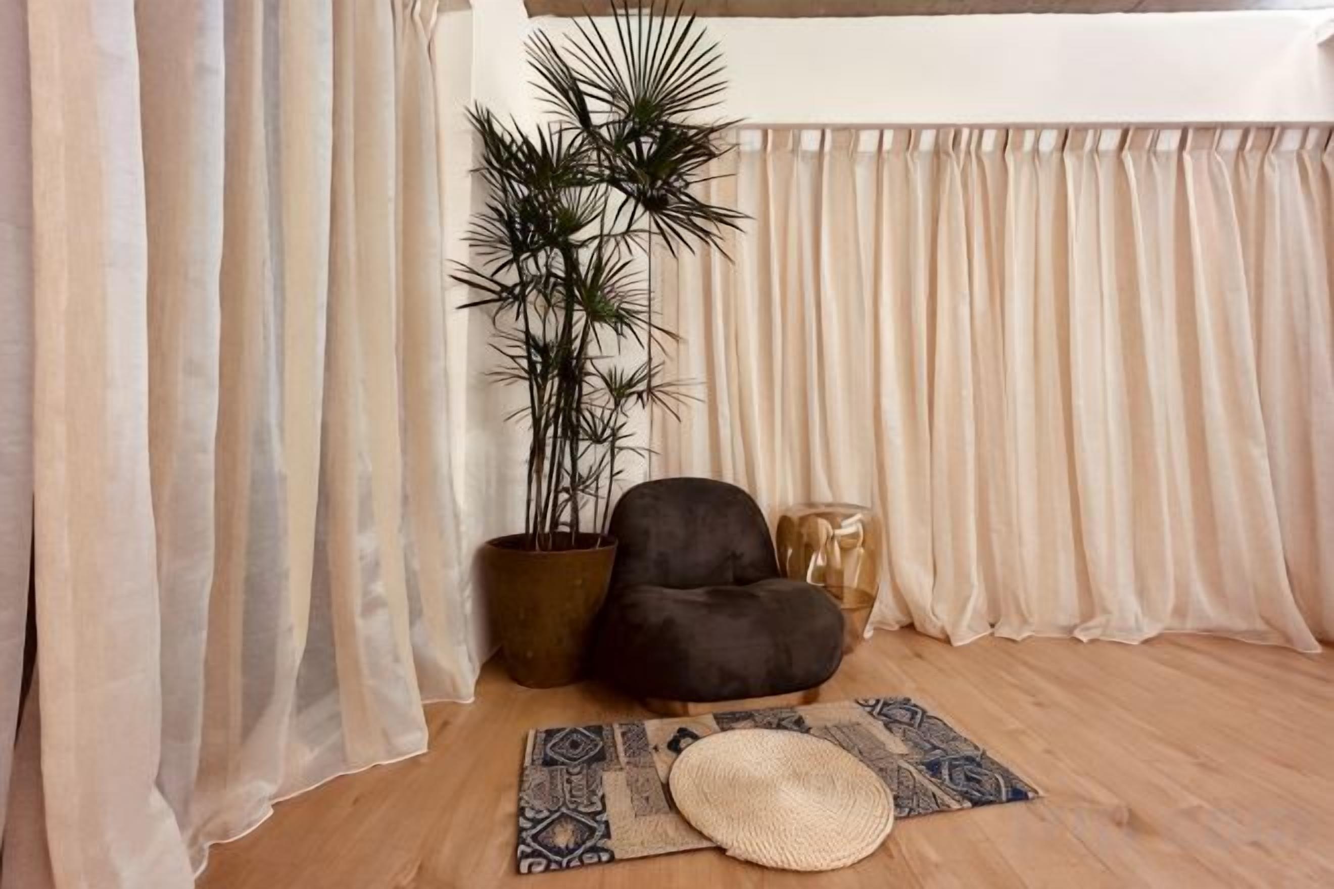 A room with a wooden floor, a black bean bag chair, a potted plant, a patterned rug, and sheer curtains.