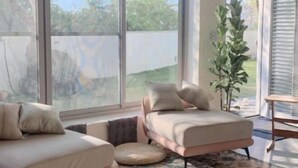 A modern living room with a sofa and armchair, large windows, and a potted plant. - Living In Light　　　　　　 (Chiayi County)