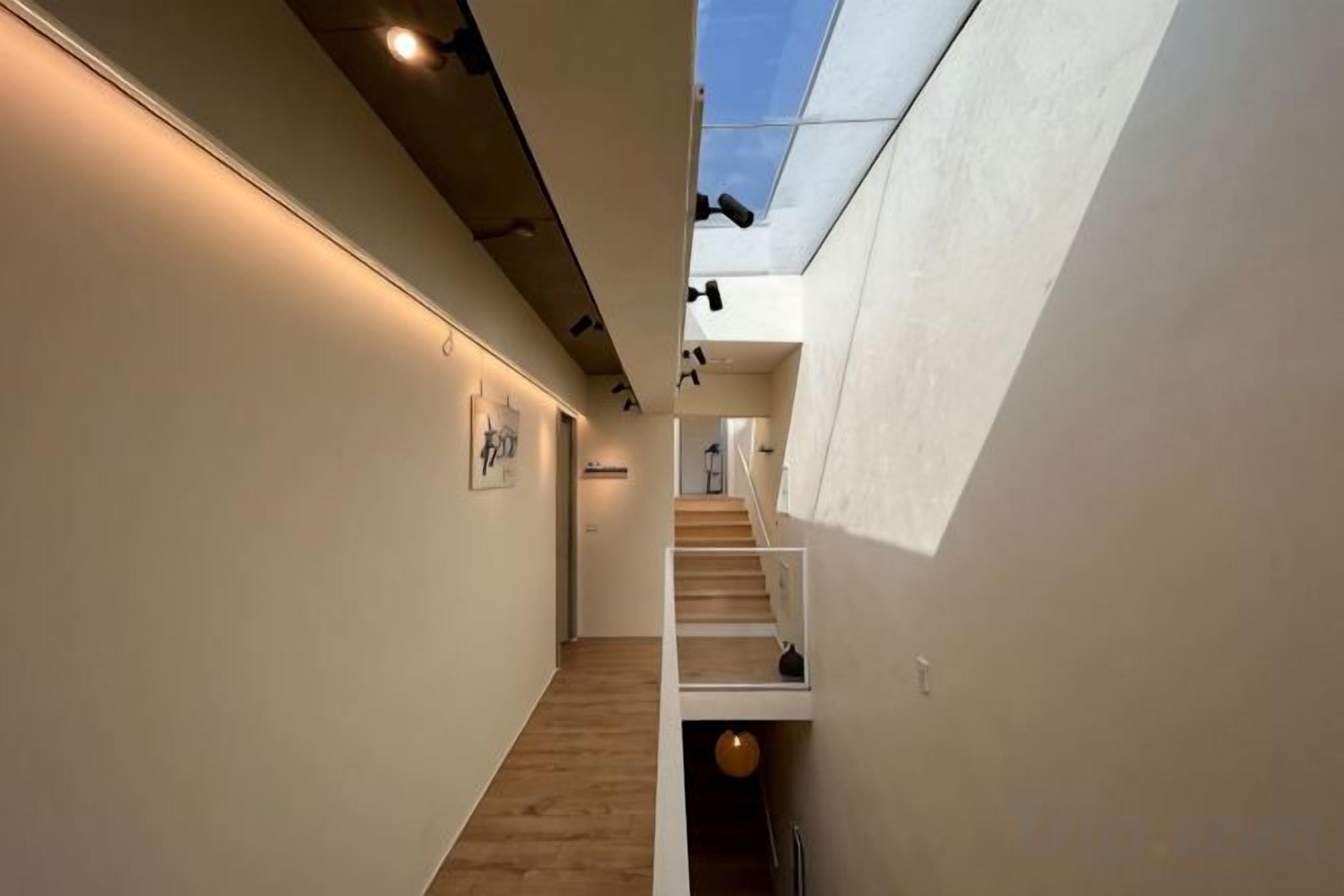A narrow hallway with a staircase leading to a second floor, a skylight, and a wall-mounted light fixture.