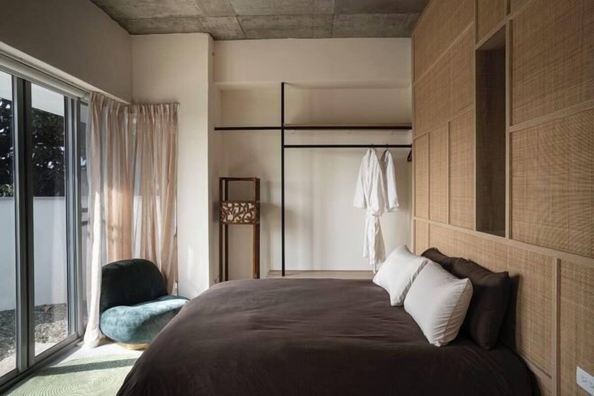 A modern bedroom with a large bed, a seating area, and a wardrobe.