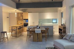 A modern kitchen with a central island, a dining area with wooden furniture, and a living space with a sofa.