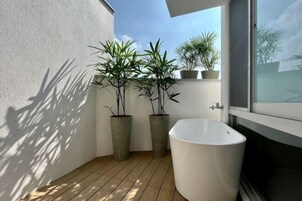 Un baño pequeño con una bañera blanca, suelo de madera y plantas en macetas.