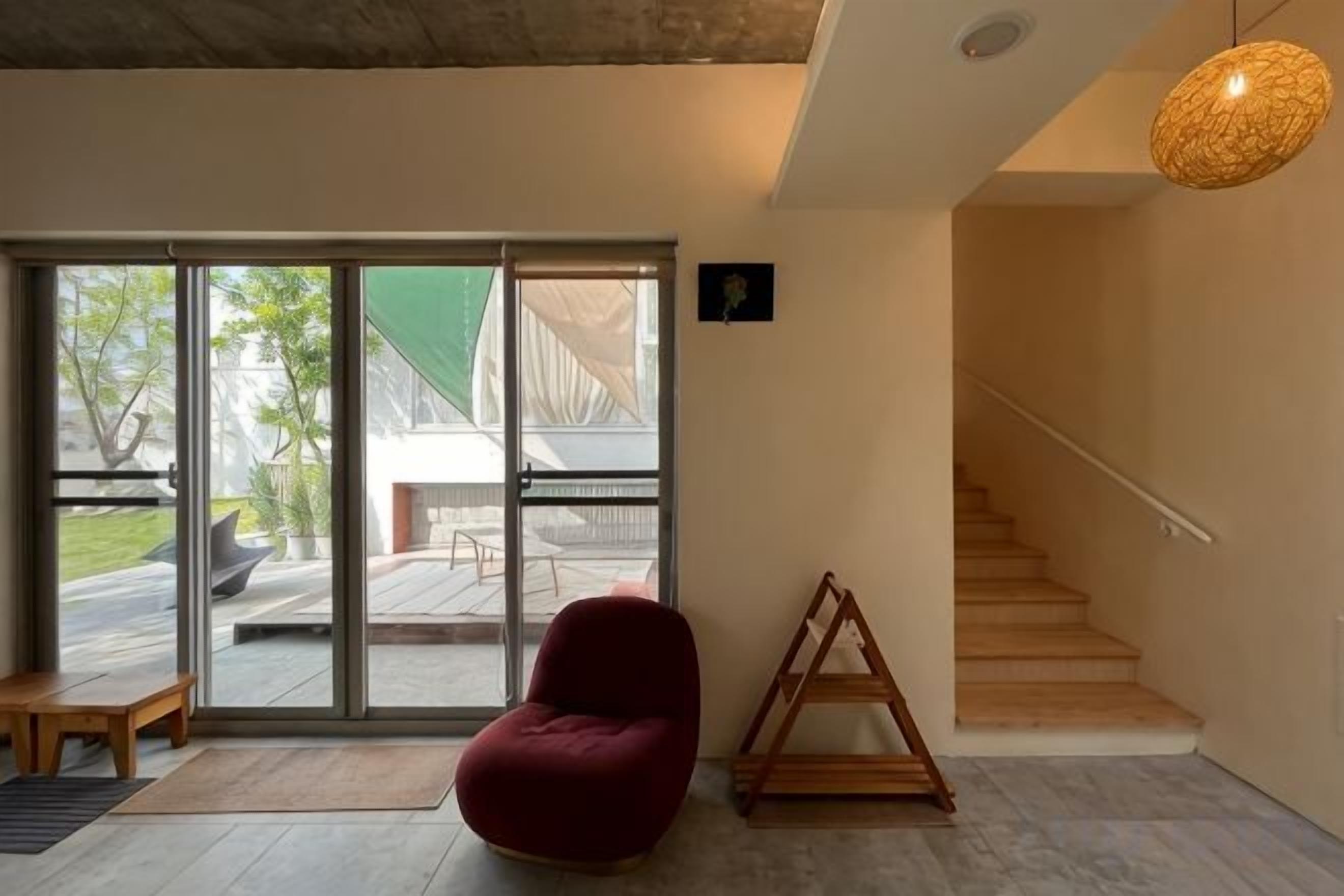 Een modern interieur met een rode stoel, een houten constructie en een trap naar een buitenruimte.