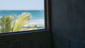 A bathroom with a large window offering a view of the ocean and palm trees. - Nimb Adobe by Wynwood House (Máncora)