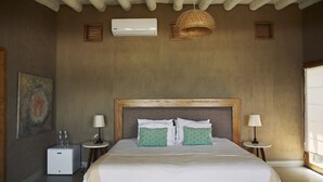 A bedroom with a large bed, two bedside tables, a wall-mounted air conditioner, a hanging light fixture, and a painting on the wall. - Nimb Adobe by Wynwood House (Máncora)