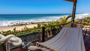 A hammock on a wooden deck overlooking a beach with waves and a clear sky. - Nimb Adobe by Wynwood House (Máncora)