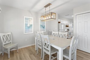 Una cocina moderna con muebles blancos, un comedor con mesa y sillas blancas, y una lámpara colgante.