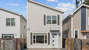 A two-story residential building with a front door, a garage door, and a small front yard with a wooden fence. - Upscale 3BR Houston I Gated Parking I Relocation I Insurance Claim I Heights (Houston)