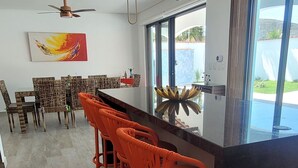 Een moderne keuken met een zwart aanrecht, oranje barkrukken en een plafondventilator.