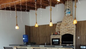 Een buitenkeuken met een bakstenen open haard, hangende verlichting en barstoelen.