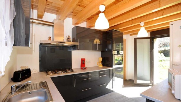 Une cuisine moderne avec des meubles de couleur noire, des appareils électroménagers en acier inoxydable et un plafond en bois.