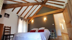 Une chambre avec un plafond en bois, un lit avec une literie blanche et des oreillers rouges, une chaise en bois et une petite table sur laquelle se trouve une bougie rouge.