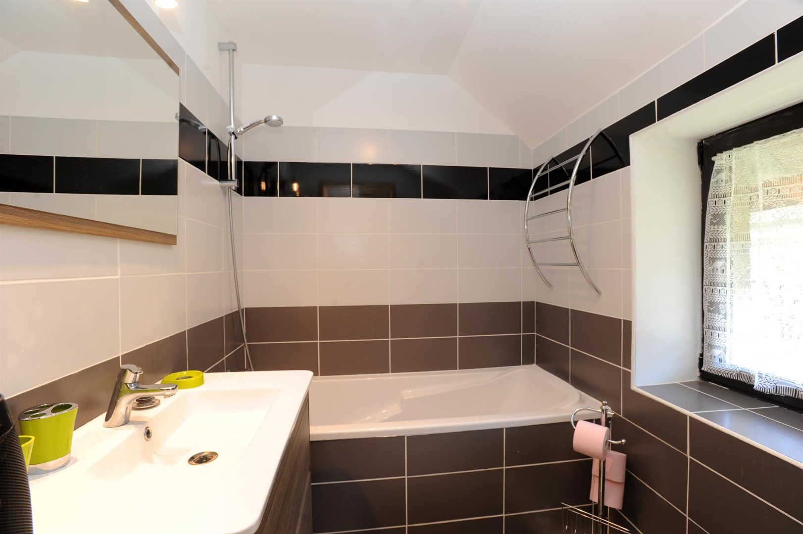 A bathroom with a bathtub, a sink, and a window with a curtain.