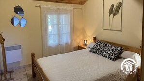 A bedroom with a wooden ceiling, a bed with a white quilt, a window with sheer curtains, and a wall-mounted radiator. - La tramontane - ELNE (ELNE)