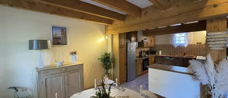 A rustic kitchen with wooden beams, a dining area with a table set for two, and a view into the adjacent dining room.