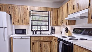 A modern kitchen with wooden cabinets, a white refrigerator, a microwave, a sink, a coffee maker, and a stove. - Casa San Gabriel Pet-Friendly Getaway Fenced w/ Fire Pit, Game Room, Kayaks (Dunnellon)
