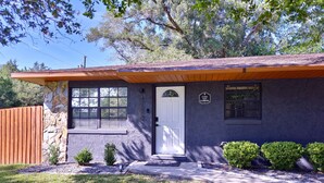 A single-story house with a stone facade, a wooden porch, a white door, and a small front yard with shrubs. - Casa San Gabriel Pet-Friendly Getaway Fenced w/ Fire Pit, Game Room, Kayaks (Dunnellon)