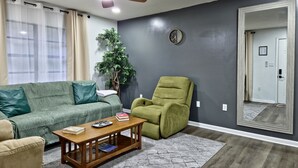A living room with a green sofa, a wooden coffee table, a green armchair, a potted plant, and a ceiling fan. - Casa San Gabriel Pet-Friendly Getaway Fenced w/ Fire Pit, Game Room, Kayaks (Dunnellon)