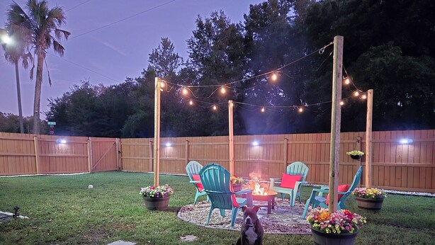 A backyard with a fire pit, outdoor chairs, and string lights. - Casa San Gabriel Pet-Friendly Getaway Fenced w/ Fire Pit, Game Room, Kayaks (Dunnellon)