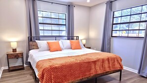A modern bedroom with a large bed, two bedside tables, and a view through the windows. - Casa San Gabriel Pet-Friendly Getaway Fenced w/ Fire Pit, Game Room, Kayaks (Dunnellon)