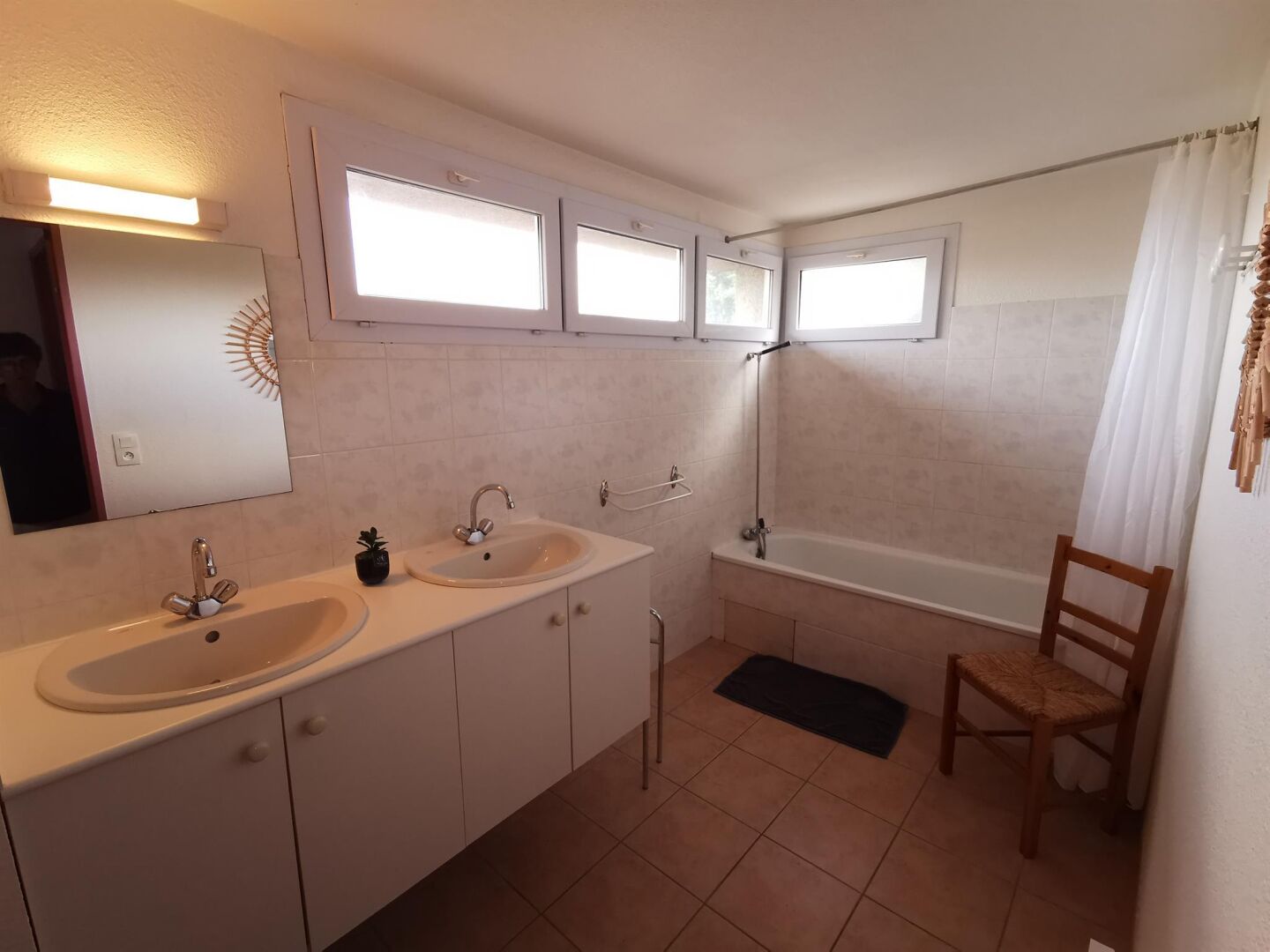 A bathroom with two sinks, a bathtub, and a shower. There are windows above the sinks and a chair near the bathtub.