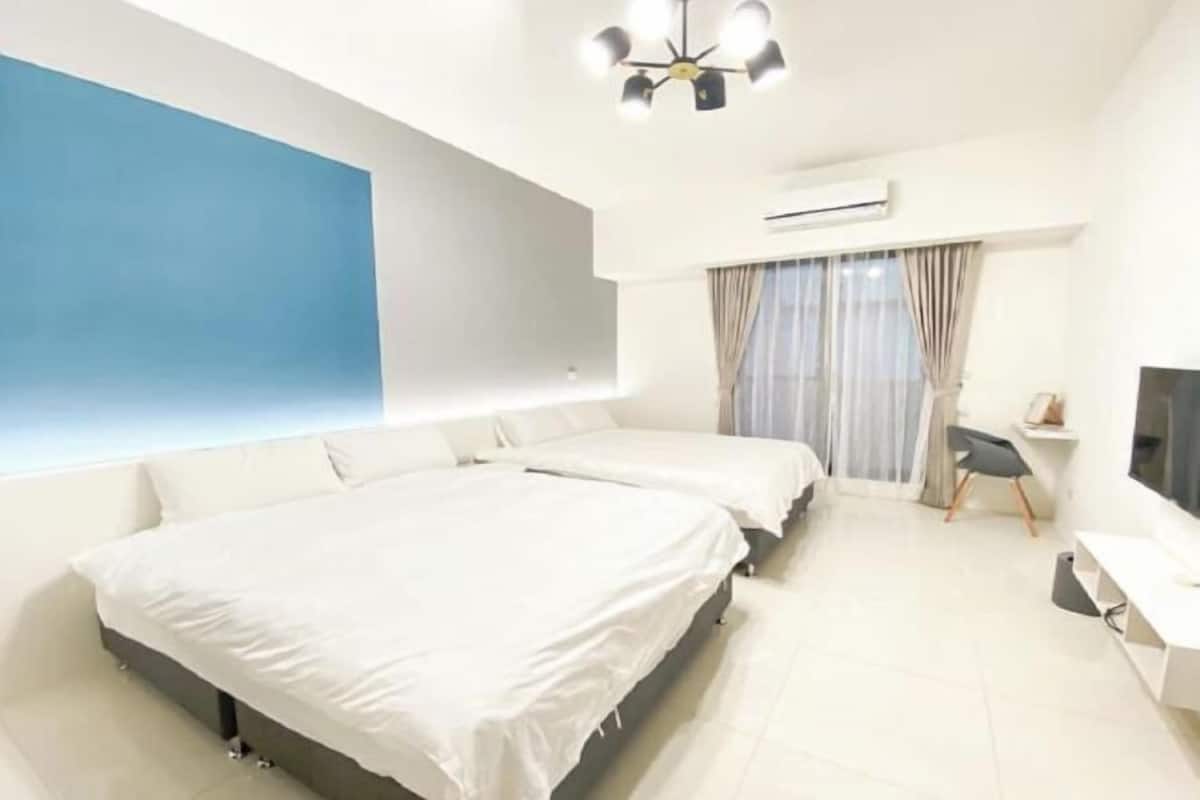 A modern hotel room with two beds, a desk, a chair, and a large window with curtains.