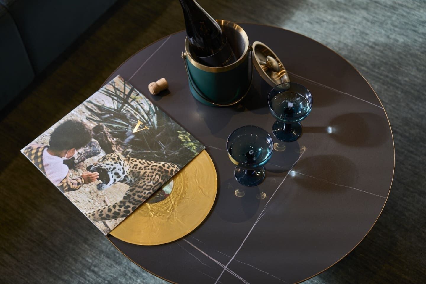 Una mesa redonda con un disco de vinilo, un corcho, un recipiente verde y tres objetos de vidrio azul.