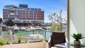 Blick von einem Balkon auf einen Hafen mit mehreren dort liegenden Booten, im Hintergrund ein modernes Gebäude mit der Aufschrift "Park Hyatt" und ein Blumentopf auf dem Balkon.