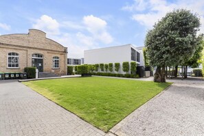 A courtyard with a lawn, a brick building, a modern white building, and a tree.
