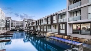 A modern hotel with a large indoor swimming pool, multiple balconies, and a clear sky. - Compact Apartment in the Heart of Lighter Quay (Auckland)