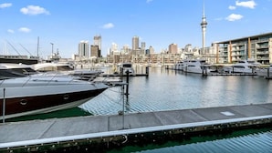 Un port de plaisance où sont amarrés des yachts, avec une vue sur les gratte-ciel de la ville en arrière-plan et une tour imposante qui se distingue.