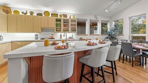 A modern kitchen with a central island, bar stools, and a dining area with chairs. - Abode at Sawtooth, chef's kitchen, sleeps 10, near ski resort (Sun Valley)