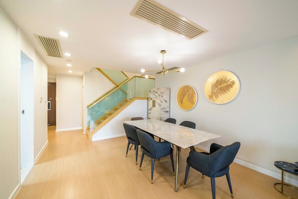 Un espace repas moderne avec une table en marbre, des chaises bleues, un escalier et des œuvres d’art décoratives sur les murs.