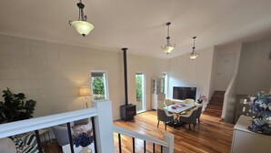 Un grand salon avec un plancher en bois, une table à manger avec des chaises, un téléviseur et une cheminée.