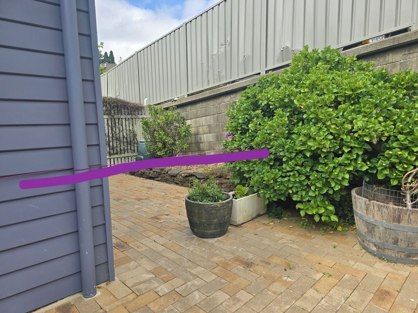Une terrasse en briques agrémentée de plantes en pot et d’une clôture en métal.