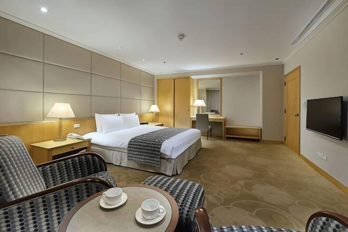 Habitación de hotel con cama, escritorio, televisión y zona de estar con dos sillas y una mesa.