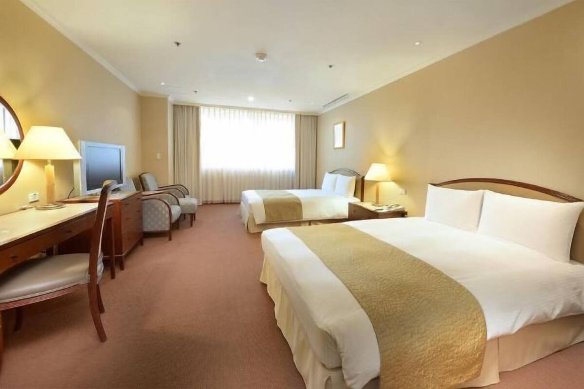 Habitación de hotel con dos camas, un escritorio, una silla, un televisor y una ventana con cortinas.