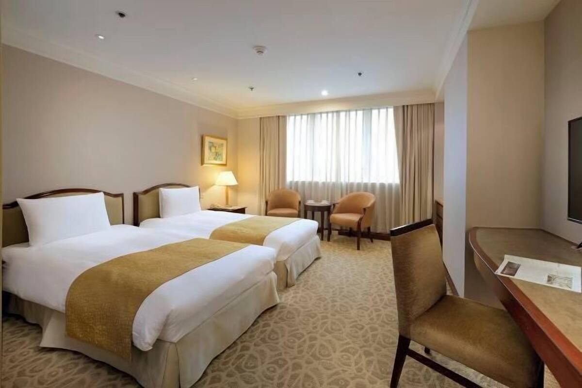 Habitación de hotel con dos camas, un escritorio, una silla, un televisor y una ventana con cortinas.