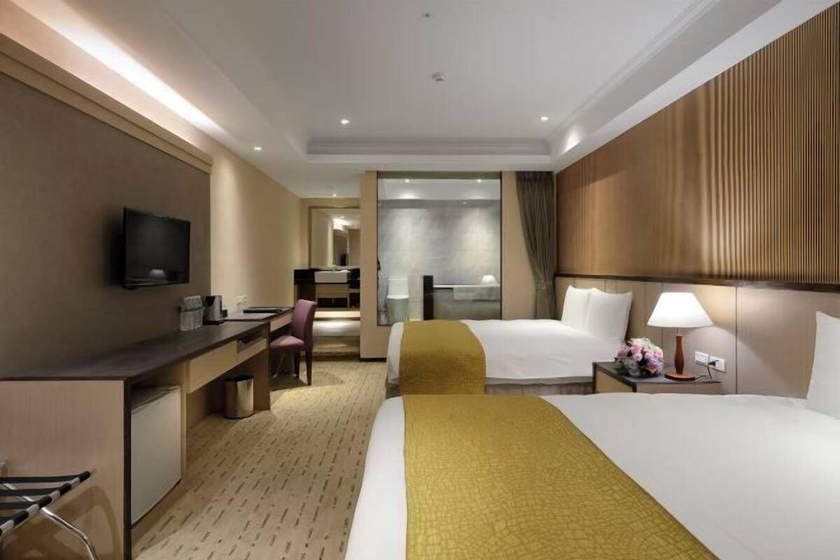 Habitación de hotel con cama, escritorio, silla, televisor y una kitchenette pequeña.
