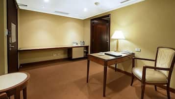 A hotel room with a bed, a desk, a chair, a lamp, and a small table.