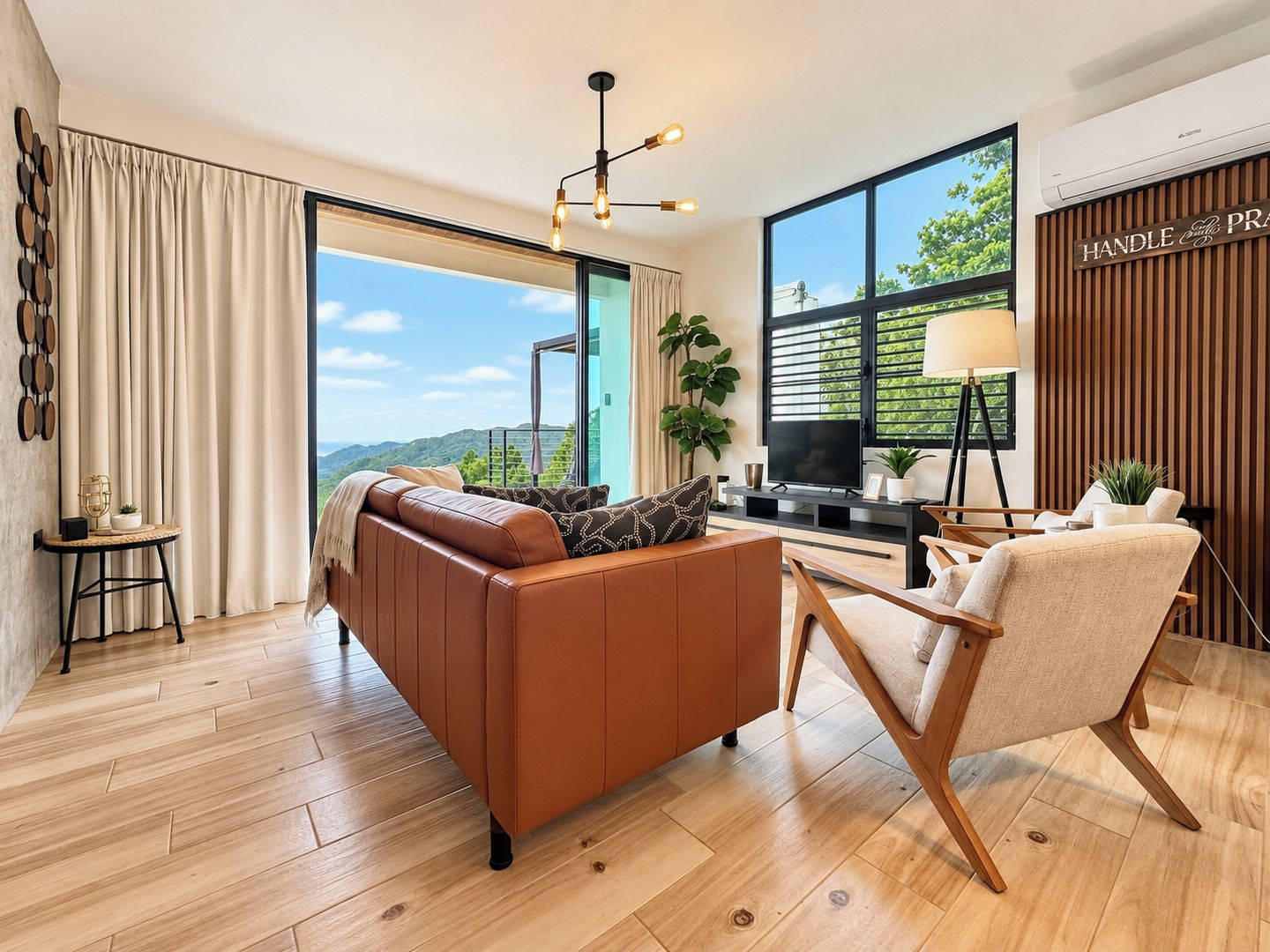 Una sala de estar moderna con un sofá de cuero, una silla de madera, un televisor y un ventanal con vistas al exterior.