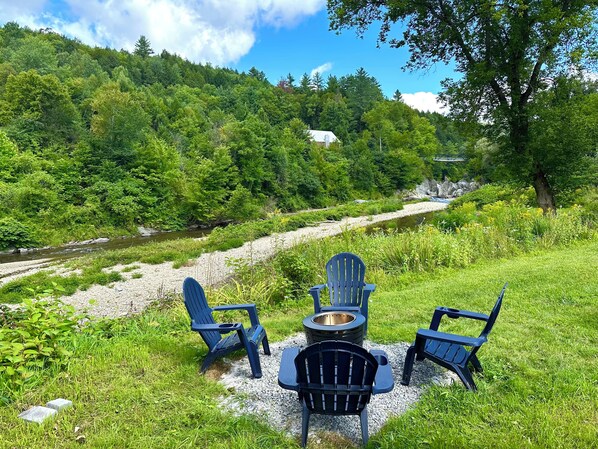 A riverside outdoor seating area with chairs and a fire pit.