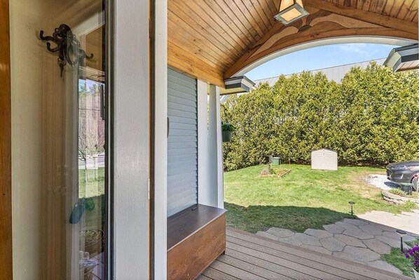 A covered porch with a wooden ceiling and a glass door.