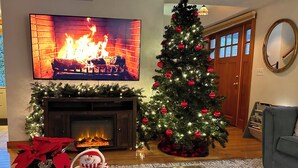 Un salon avec une cheminée, un sapin de Noël et un téléviseur fixé au mur.