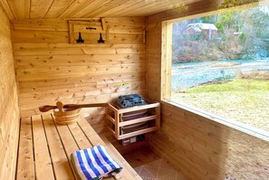 A wooden sauna room with a bench, a wooden bucket, and a rack for towels.