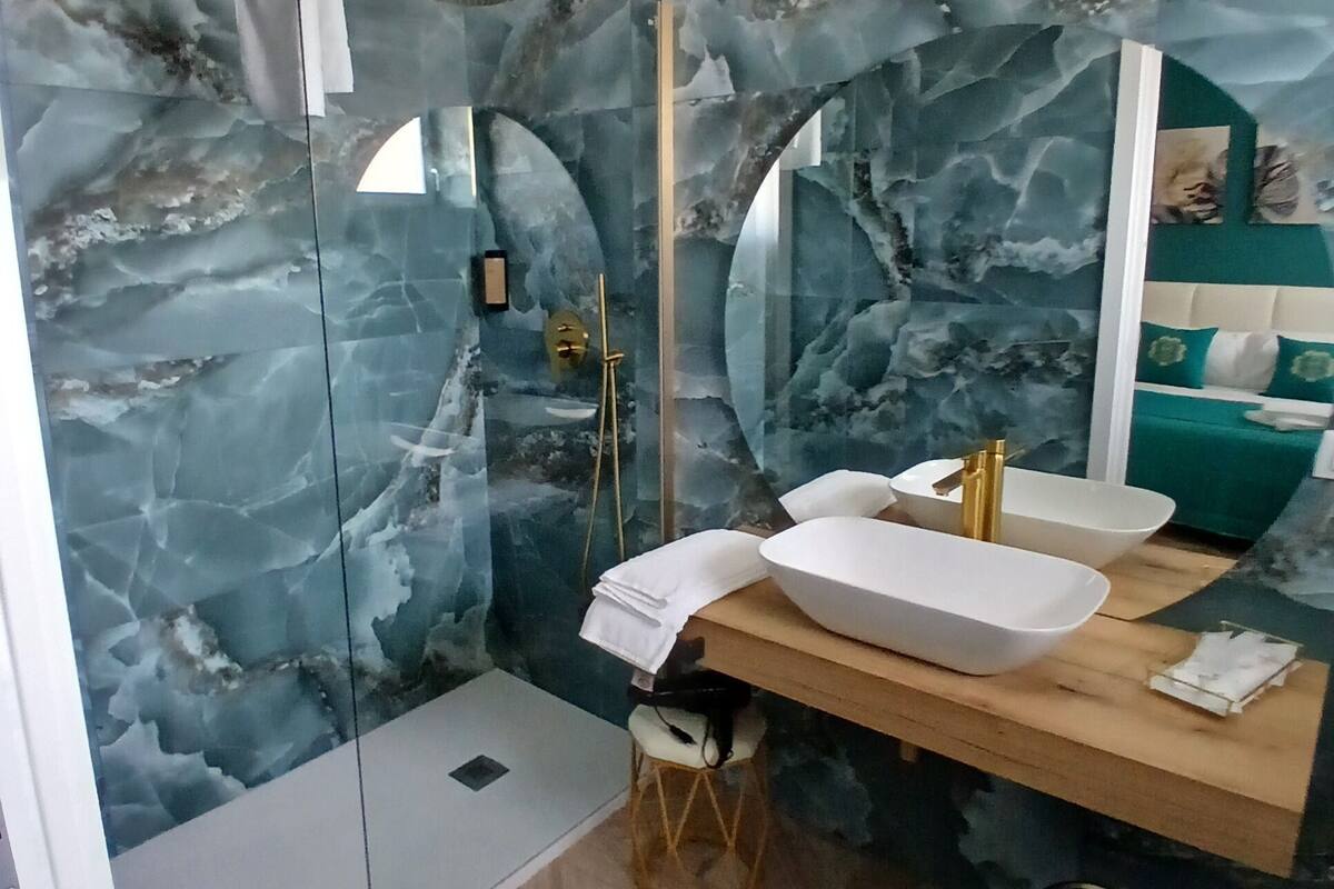 Ein modernes Badezimmer mit Marmorwandgestaltung, einer Glasdusche, einem Holzmöbelkorpus mit weißem Waschbecken und einem Spiegel.