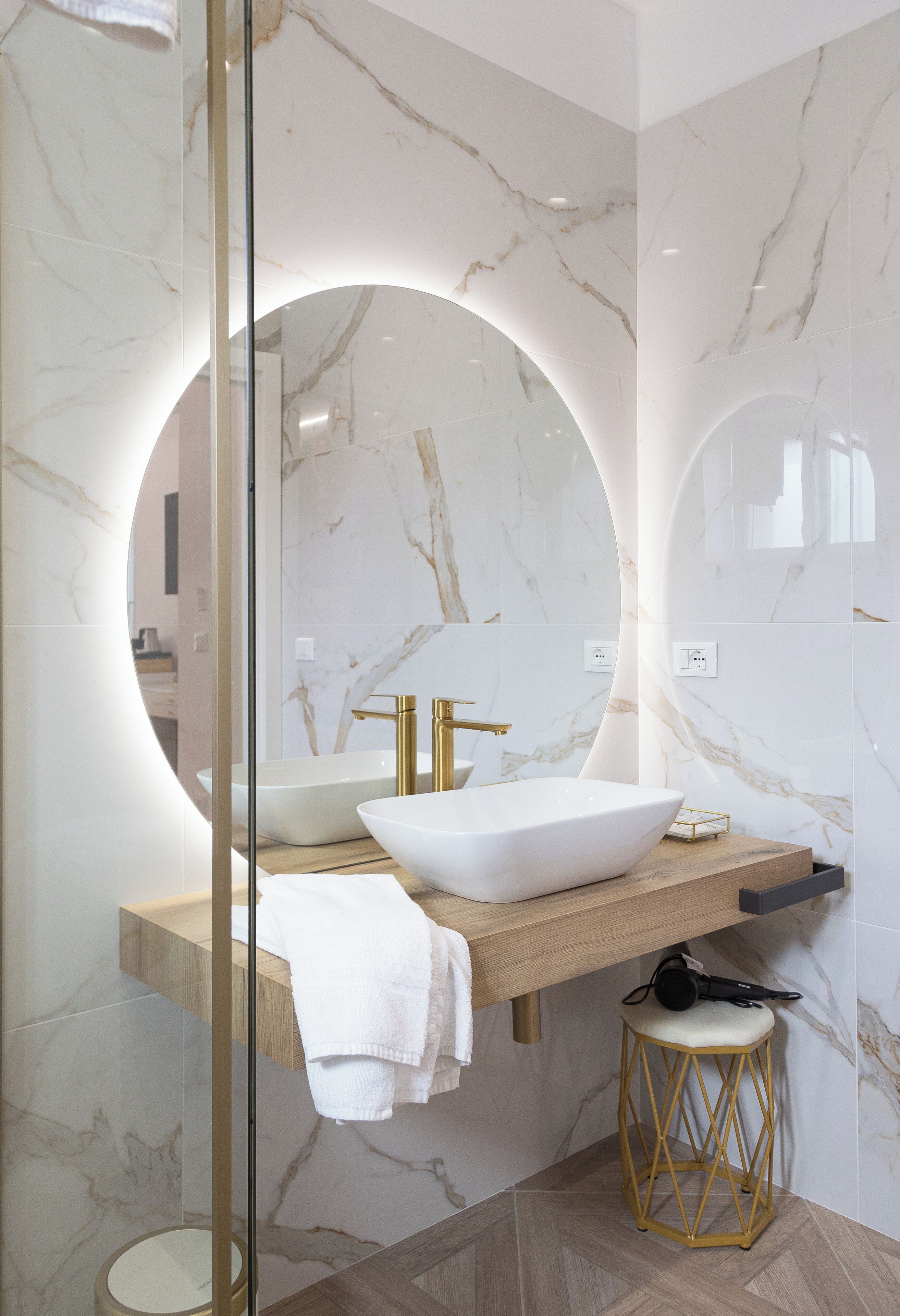 A modern bathroom with a large oval mirror, a vessel sink, and a gold faucet.