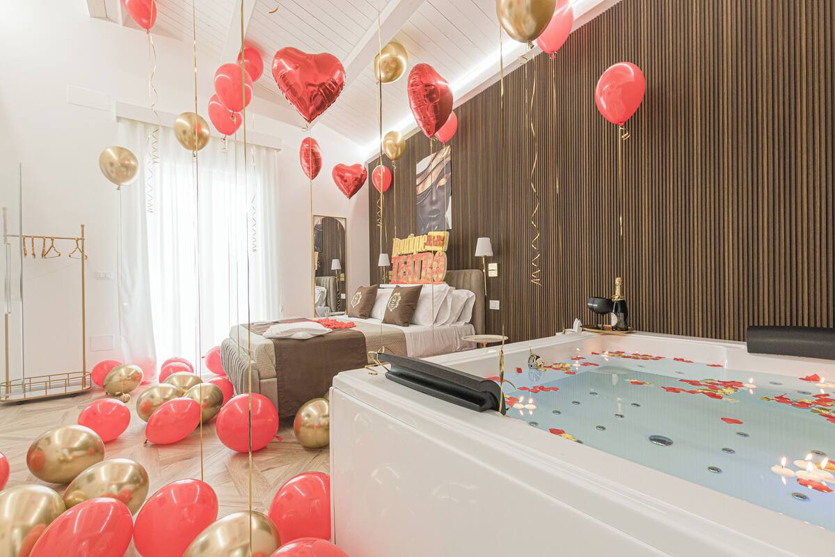 Ein Zimmer mit einer großen Badewanne, einem Sofa und einem Bett. Luftballons und ein Schild mit der Aufschrift 'Happy Birthday'.
