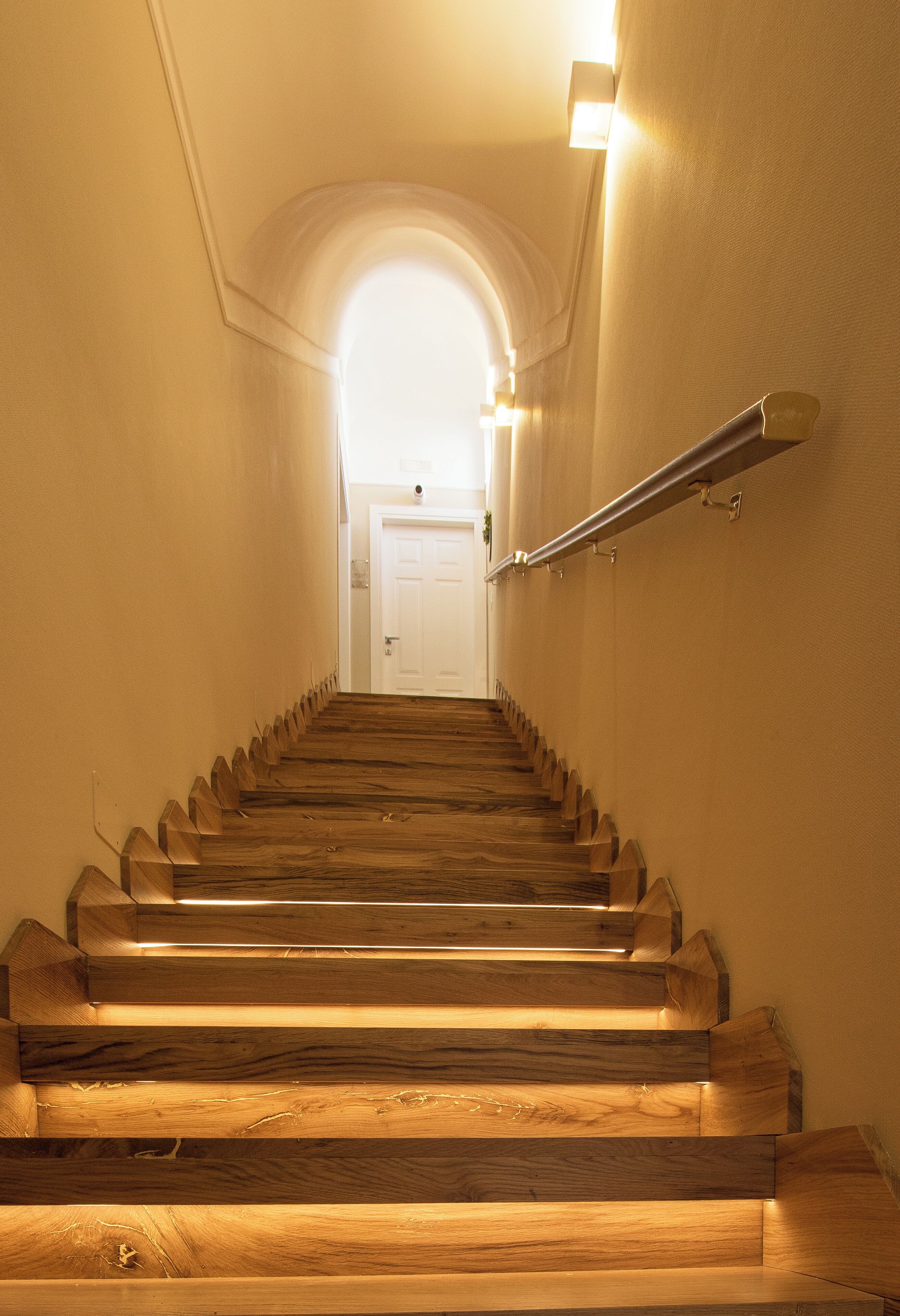 Un escalier en bois, doté d’une rampe, mène à une porte blanche située en haut.