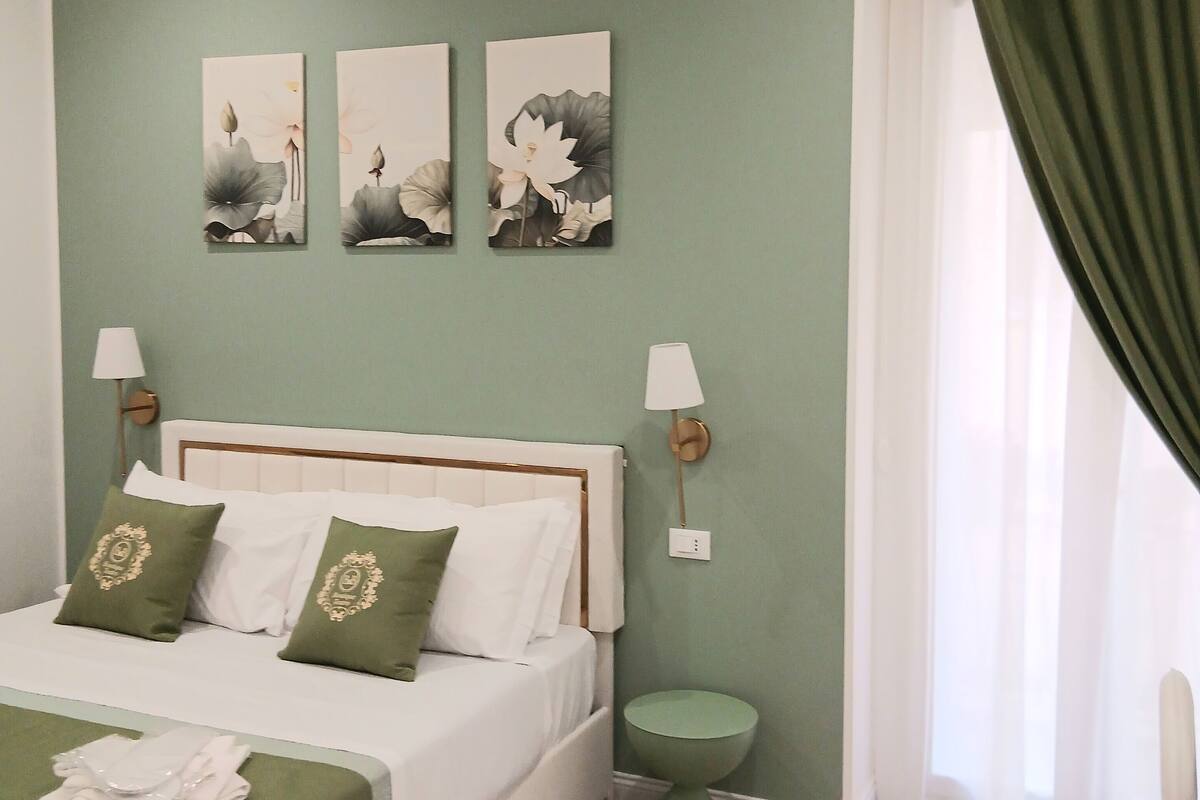 Ein ordentlich eingerichtetes Schlafzimmer mit einem Bett, Kissen, einem Nachttisch und Wandbildern.